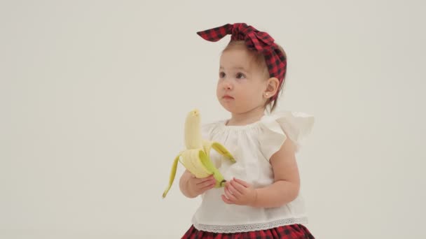 Een Meisje Met Een Geruite Hoofdband Heeft Een Geschilde Banaan — Stockvideo