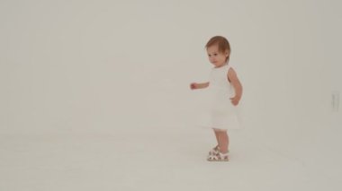 Little girl in dress is playing on the white carpet. Slow motion.