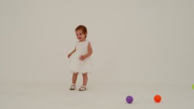 Little girl in dress is playing on the white carpet. Slow motion.