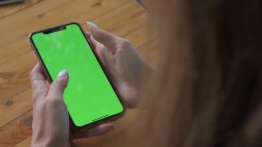Womans hands hold smartphone which screen is lights up green. Filmed outdoors
