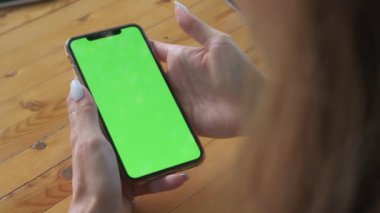 Womans hands hold smartphone which screen is lights up green. Filmed outdoors