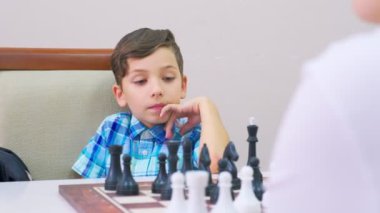 Mavi kareli gömlekli çocuk satranç oynar. Arkadaki ışık duvarı, yakın plan, tahta satranç tahtası..