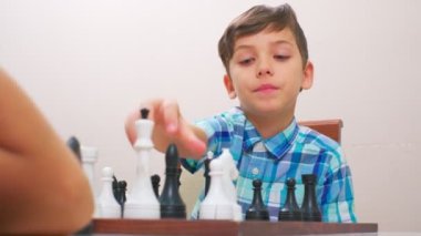 Mavi kareli gömlekli çocuk satranç oynar. Arkadaki ışık duvarı, yakın plan, tahta satranç tahtası..