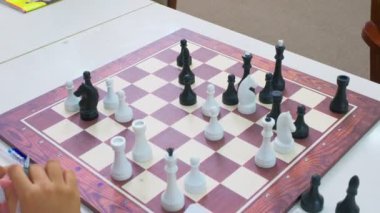 Çocuklar satranç oynuyorlar. Tahta tahtaya yakın çekim. Hareket eden kamera, el ele tutuşan kalem satranç hamlesi yapıyor.