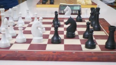 Çocuklar satranç oynuyorlar. Beyaz masadaki tahta satranç tahtası yan tarafından çekildi. Yakın çekim, satranç taşları değiş tokuşu, kamera hareketleri izliyor.