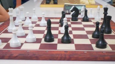 Çocuklar satranç oynuyorlar. Beyaz masadaki tahta satranç tahtası yan tarafından çekildi. Yakın çekim, kamera hareketleri izler.