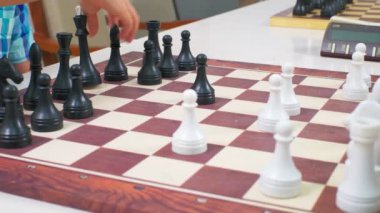 Çocuklar satranç oynuyorlar. Beyaz masadaki tahta satranç tahtası yan tarafından çekildi. Yakın çekim, kamera hareketleri izler.