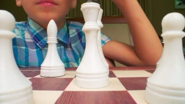 チェスの数字はチェス盤の極端なクローズアップ 青い頬のシャツの少年は背中にチェスをしている 取締役会のレベルで側面から撮影 — ストック動画
