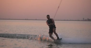 Wakesurfer gölde sörf tahtası kullanıyor. Yakın çekim, deniz mavisi wakeboard, günbatımında çekilmiş..