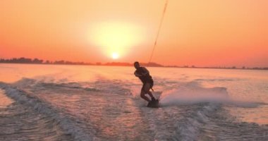 Wakesurfer gölde sörf tahtası kullanıyor. Yakın çekim, deniz mavisi wakeboard, günbatımında çekilmiş..