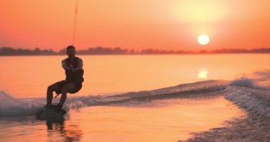 Wakesurfer gölde sörf tahtası kullanıyor. Yakın çekim, deniz mavisi wakeboard, günbatımında çekilmiş..