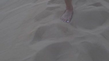 Dubai çölünde kum tepeciğinde yatan bir kızın ayakları. Ağır çekim, yakın çekim..