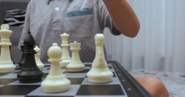 Gri tişört giyen çocuk satranç dönüşünü yapıyor. - Yakın çekim. Satranç tahtası seviyesinde çekildi..