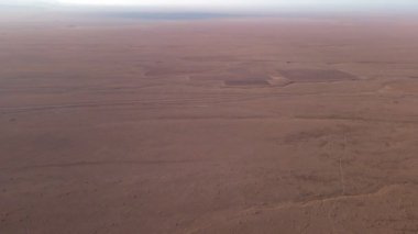 Güneşli bir günde, çöldeki kurumuş nehir yatağının üzerinden bir drone geçiyor.