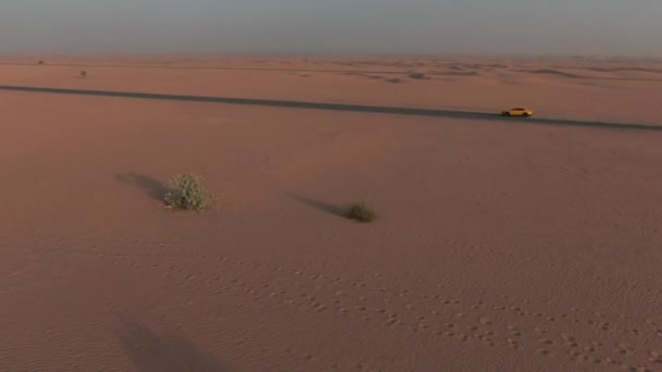 砂漠の砂丘の間の砂で満たされた道路に沿って運転する車の後ろの無人機 — ストック動画