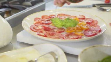 Şef domates ve yeşil salataya zeytinyağı ekliyor, yavaş çekimde yakın plan.