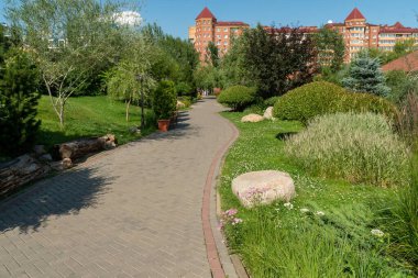 Güneşli bir yaz gününde süs bitkileri arasındaki esnek bir yol parktan konut binalarına çıkar..