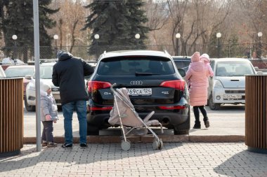 Krasnoyarsk, Krasnoyarsk Bölgesi, RF - 14 Mart 2021: Güneşli bir bahar gününde, park halindeki bir arabanın yanında iki çocuklu genç bir aile.