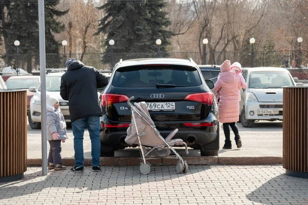 Krasnoyarsk, Krasnoyarsk Bölgesi, RF - 14 Mart 2021: Güneşli bir bahar gününde, park halindeki bir arabanın yanında iki çocuklu genç bir aile.