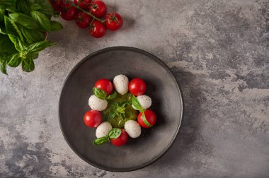 Düz İtalyan caprese salatası, olgun domates, taze fesleğen ve siyah tabakta mozzarella peyniri.