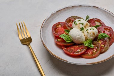 Kırmızı domatesli Caprese salatası, fesleğen ve mozzarella peyniri ve altın çatal.