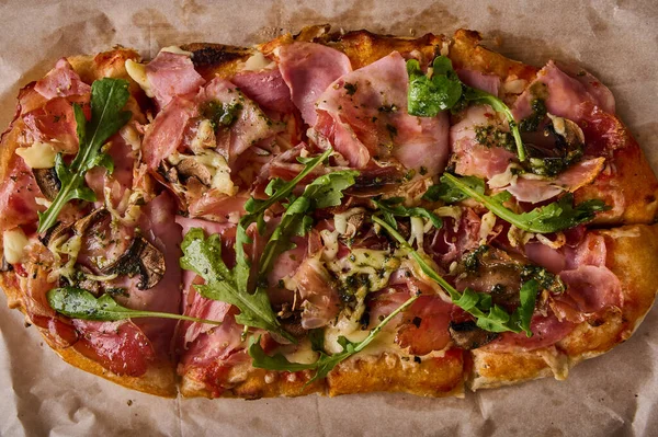 Traditional rectangular Roman pizza with prosciuto ham, tomatoes, mozzarella, mushrooms and arugula