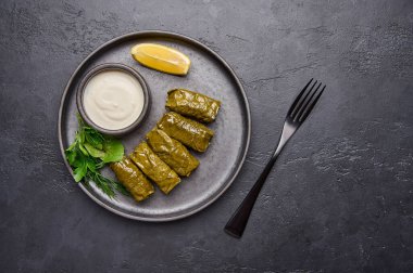 Dolma, maydanoz, ekşi kremalı tencere ve siyah tabakta limon.