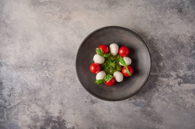 Olgun domatesli İtalyan caprese salatası taze fesleğen ve siyah tabakta mozzarella peyniri.