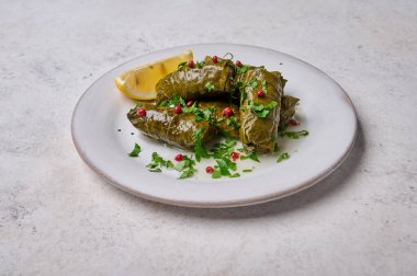 Stuffed grape leaves with rice, meat, parsley, pepper and lemon in white plate. Top view dolma. Light wooden background, close up clipart
