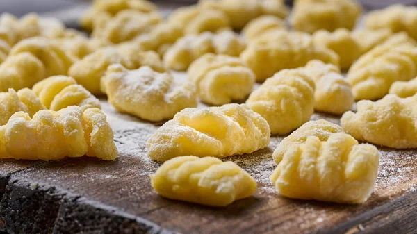 Homemade uncooked potato gnocchi with flour and grated parmesan cheese over wooden cutting board. Macro, selective focus — Stock Photo, Image