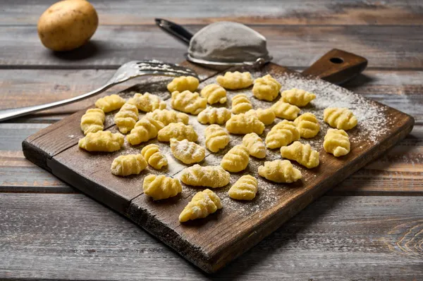 Gnocchi crudo sin cocer de papa, tamiz y tenedor en tabla de cortar de madera en mesa rústica —  Fotos de Stock