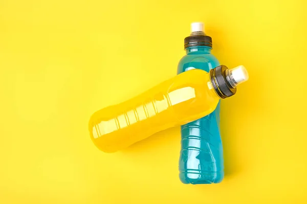 Isotonic energy yellow and blue sport drink in plastic bottles on yellow background. Top view, copy space