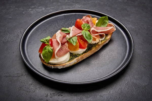 Tutup bruschetta dengan mozzarella, Parma ham dan pesto di piring hitam Stok Gambar Bebas Royalti