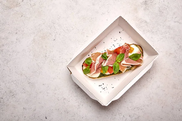 Top vista bruschetta com mussarela, presunto Parma e pesto em recipiente de papelão branco sobre fundo claro Fotos De Bancos De Imagens Sem Royalties