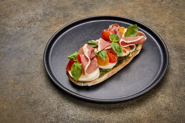 Tutup bruschetta dengan mozzarella, Parma ham dan pesto di piring hitam Stok Foto Bebas Royalti