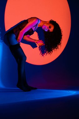 Siyah iç çamaşırı ve pantolon askılı çoraplı baştan çıkarıcı genç manken. Stüdyoda iç çamaşırlı, kıvırcık saçlı, neon ışıklı, şehvetli bir kadın..