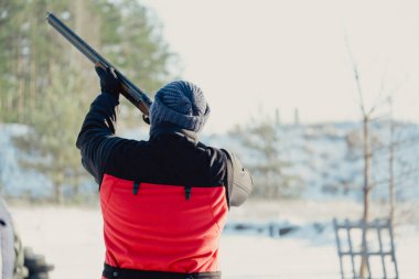 Kış ormanında av tüfeğiyle kamuflajlı avcı. Av kavramı. Karlı bir günde rezerv alan bir adam. Avcı karlı ormandaki bir silahtan nişan alıyor.
