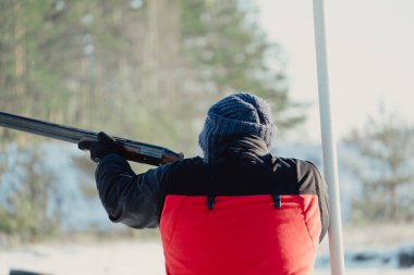 Kış ormanında av tüfeğiyle kamuflajlı avcı. Av kavramı. Karlı bir günde rezerv alan bir adam. Avcı karlı ormandaki bir silahtan nişan alıyor.
