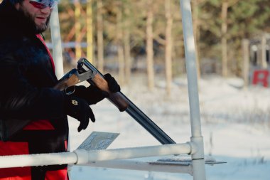 Kış ormanında av tüfeğiyle kamuflajlı avcı. Av kavramı. Karlı bir günde rezerv alan bir adam. Avcı karlı ormandaki bir silahtan nişan alıyor.