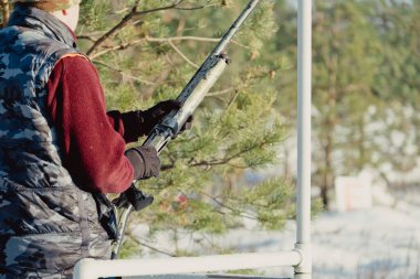 Kış ormanında av tüfeğiyle kamuflajlı avcı. Av kavramı. Karlı bir günde rezerv alan bir adam. Avcı karlı ormandaki bir silahtan nişan alıyor.