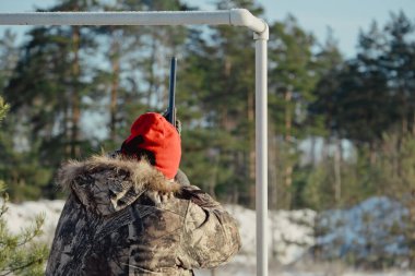 Kış ormanında av tüfeğiyle kamuflajlı avcı. Av kavramı. Karlı bir günde rezerv alan bir adam. Avcı karlı ormandaki bir silahtan nişan alıyor.