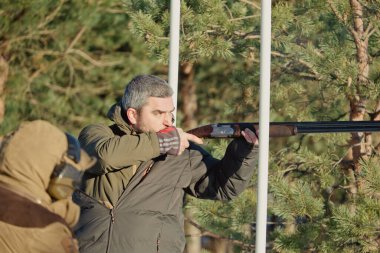 Tuzak ya da hedef atışı, kamuflajlı sporcu kil güvercine pompalı tüfekle ateş ediyor, yarışmalarda ormanın ve gökyüzünün arka planı. Rusya, Ryazan '11 Aralık 2021