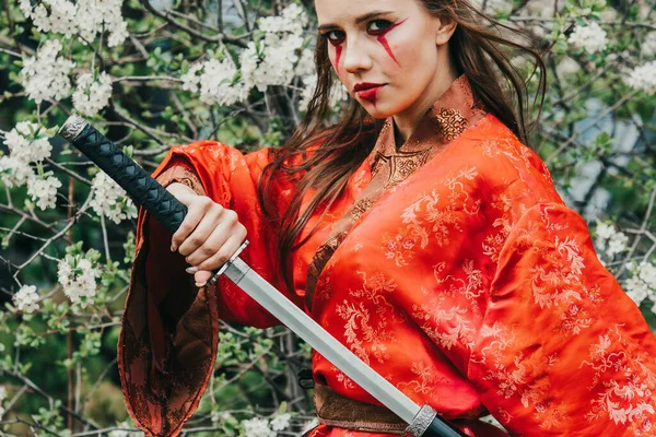 Geleneksel kimano giymiş genç bir kız çiçek açan bahçesinde Japon samuray kılıcı katana ile savaşçı kadın suretinde.