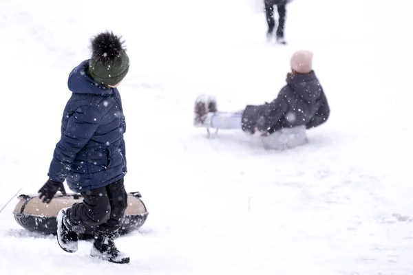 어두운 작업복을 겨울에는 아이들이 겨울에는 공원에서 있었습니다 소년은 튜브로 미끄럼틀을 스톡 사진