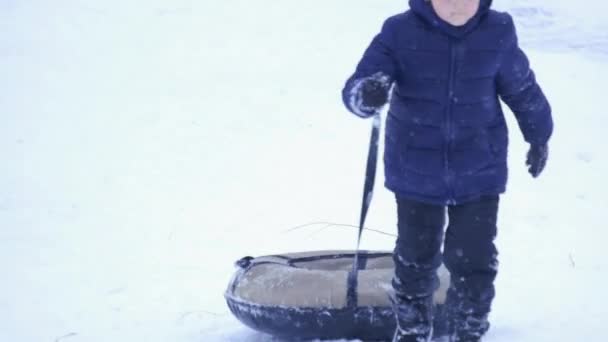 Egy Csinos Kisfiú Sötét Overálban Lecsúszik Egy Jégcsúszdán Téli Gyerekjátékokon — Stock videók