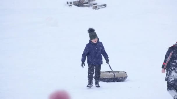 어두운 작업복을 겨울에는 아이들이 겨울에는 공원에서 있었습니다 소년은 튜브로 미끄럼틀을 — 비디오