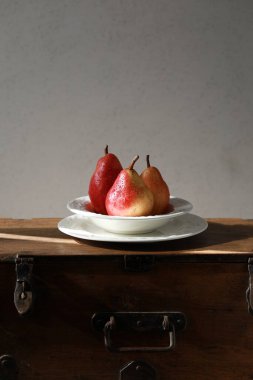 Armutlar. Ahşap zemin üzerinde porselen bir tabakta üç armut. Kırsal biçim. 