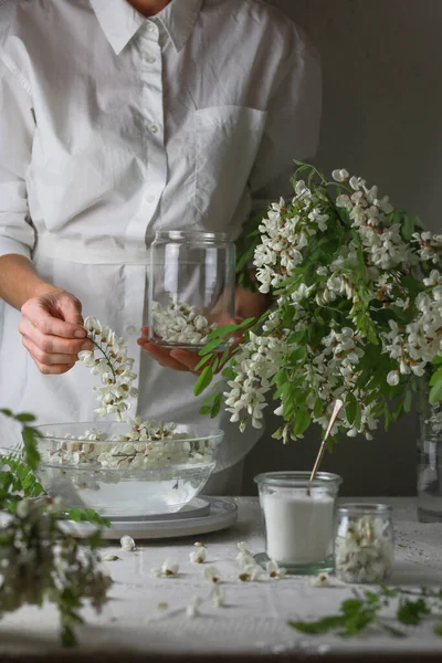 Frau in weißem Kleid legte Akazienblumen in einen Teller mit Wasser. Mädchen bereitet Akazienmarmelade zu. — Stockfoto