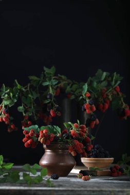 Mulberry berries on the branches. Fresh mulberries in a vase on dark background. Dark mood photo. Copy space. 