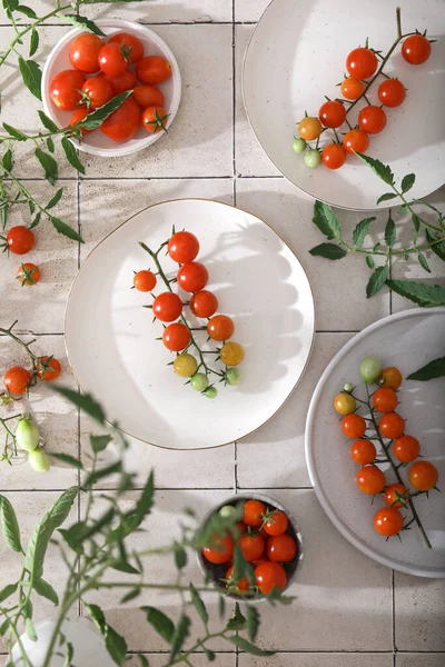 Fresh red cherry tomatoes on branch on white plates.